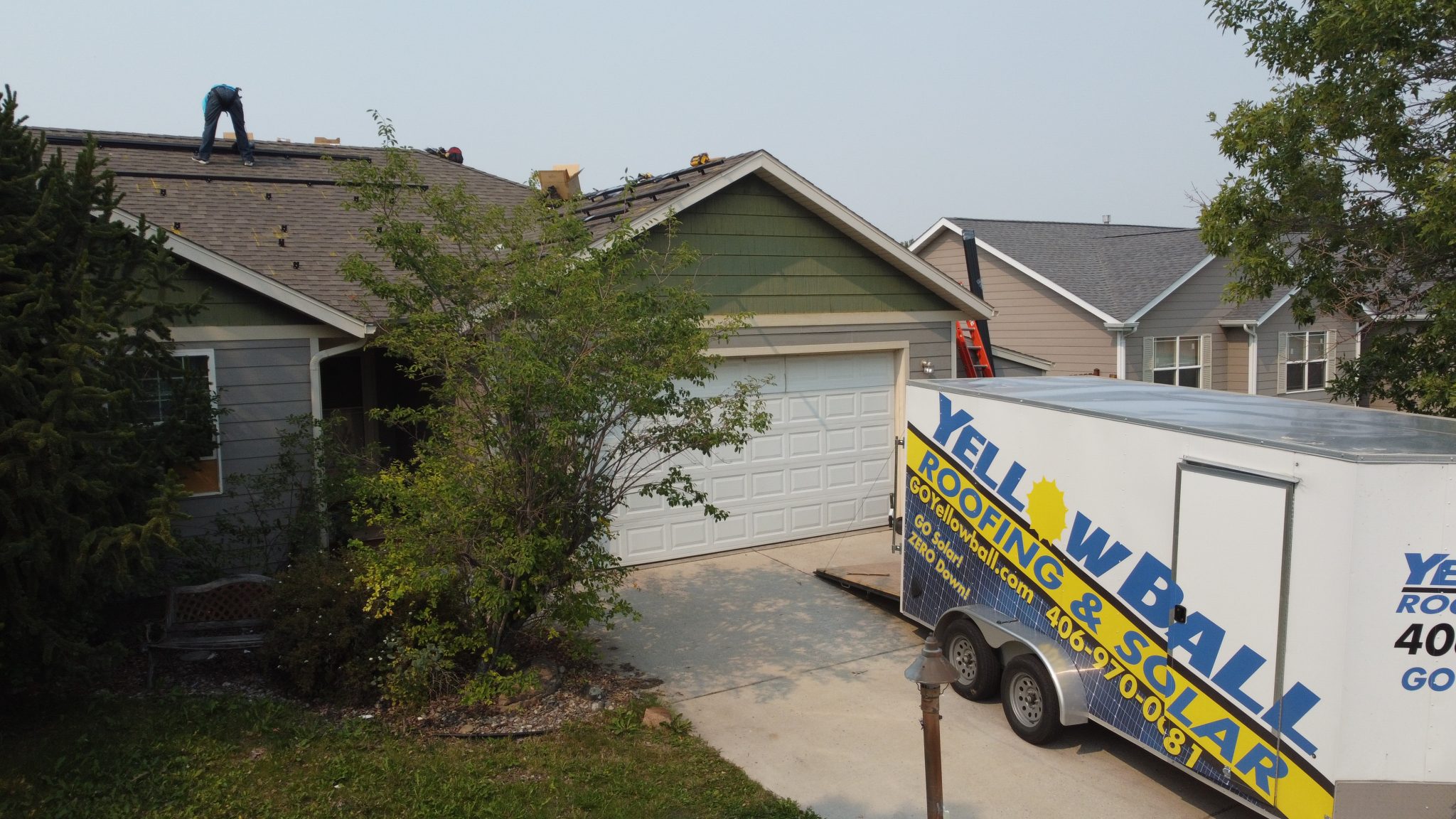 YellowBall Roofing & Solar trailer parked in front of a home while workers perform roofing services in Bozeman on a residential roof.